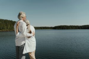 A senior couple sharing a loving embrace by a serene lakeside, symbolizing enduring love.